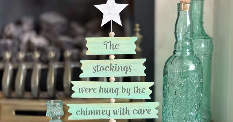 Wooden tree decoration painted light green, with painted text reading 'the stockings were hung by the chimney with care'
