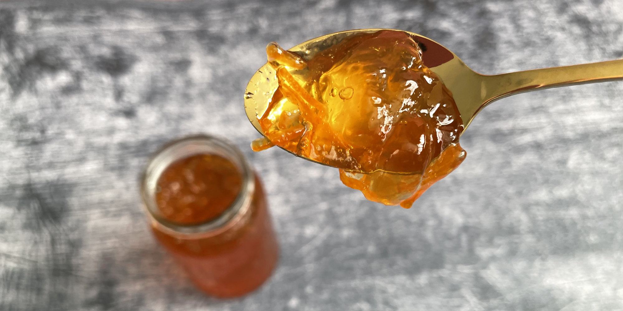 marmalade on a golden spoon, top down, with an open jar of marmalade in the background