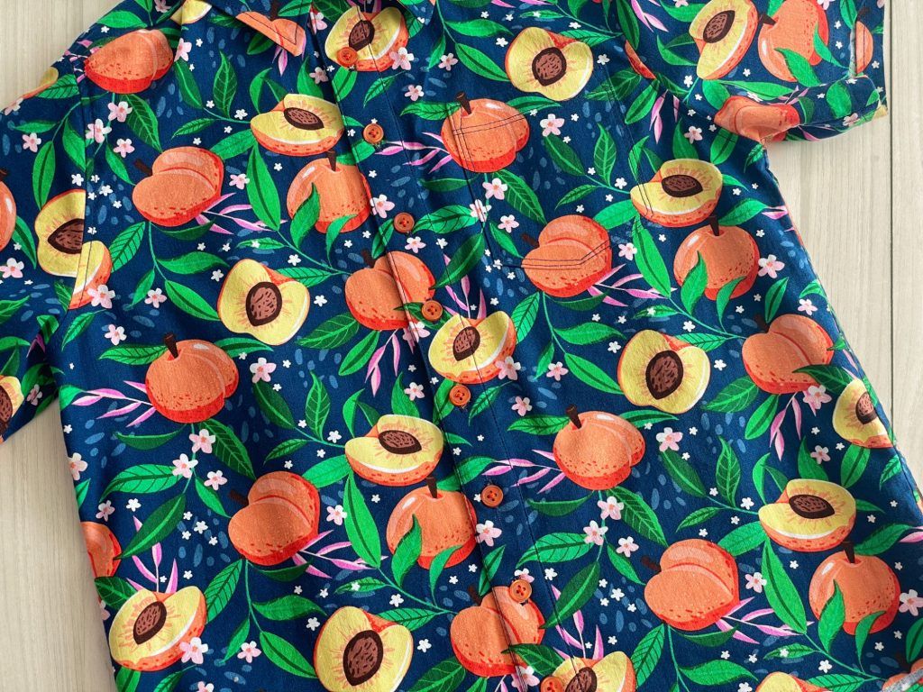 close up of a short sleeved aloha style shirt with a peach graphic print.